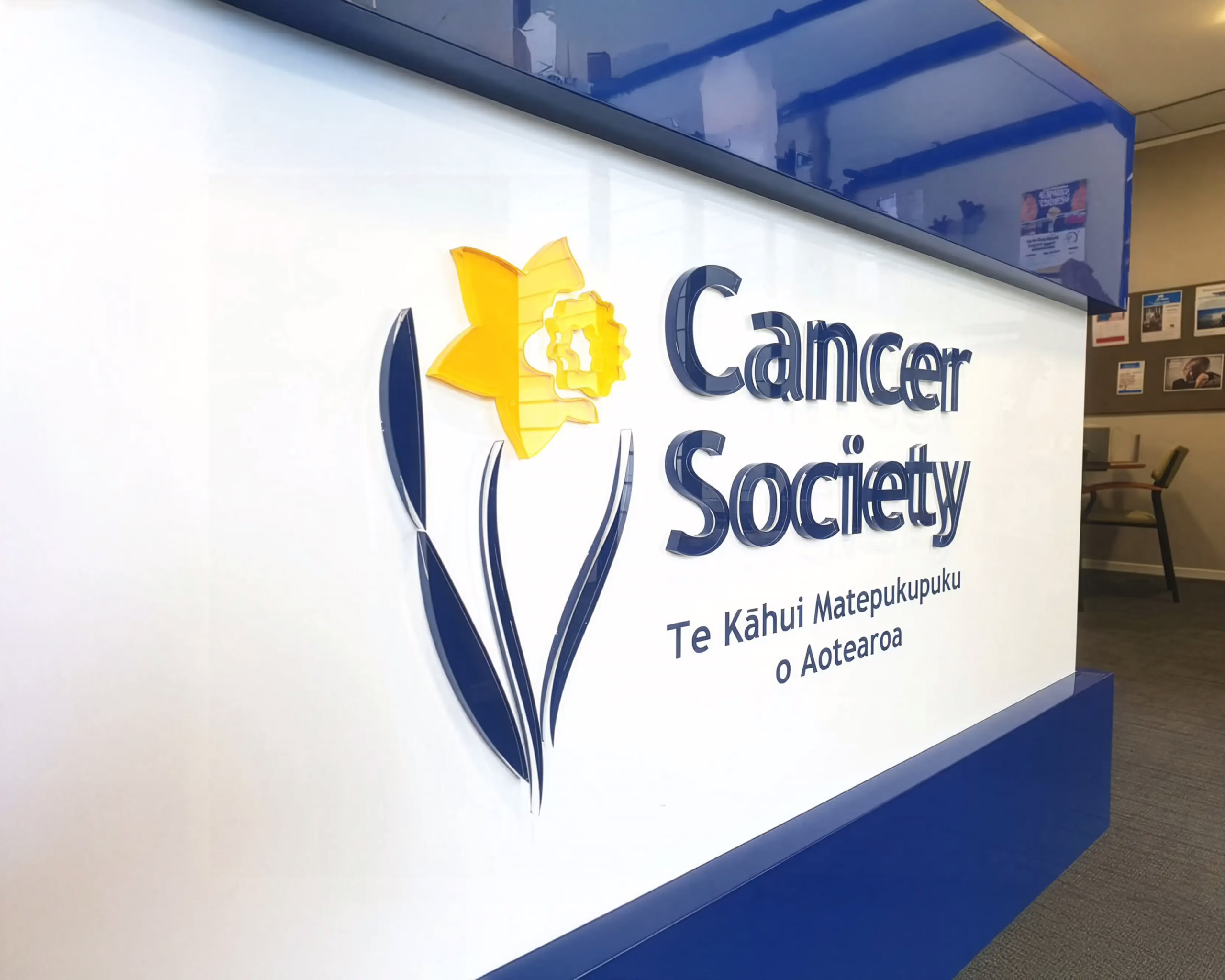 3D acrylic Cancer Society sign with yellow daffodil logo mounted on a white wall by Timaru Signs Graphix.