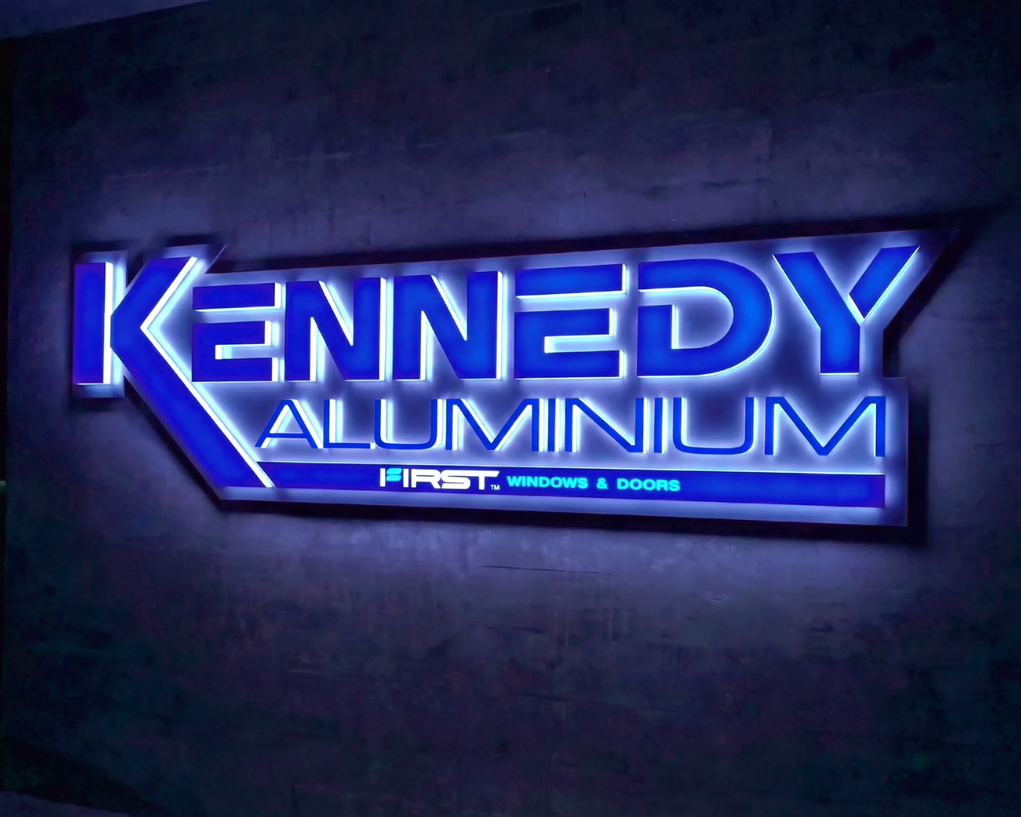 Illuminated blue halo-lit 3D custom signage for Kennedy Aluminium, installed on a dark textured wall in Timaru.