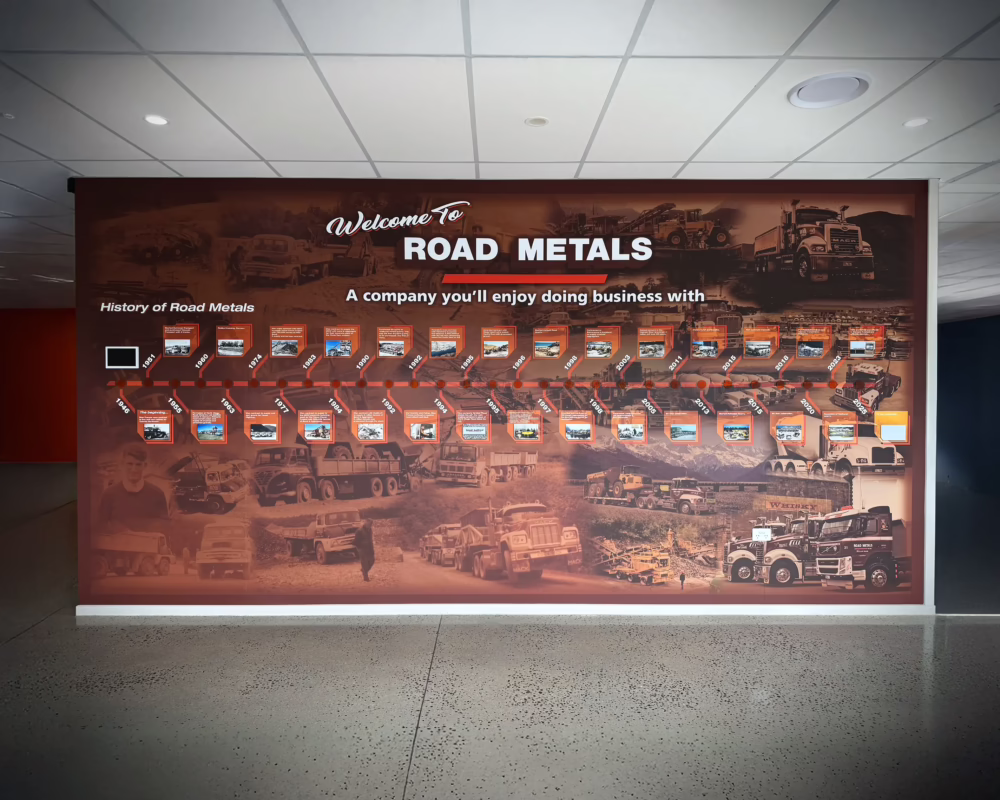 Custom history wall graphics for Road Metals by Timaru Signs, featuring a timeline and vintage photo collage on a polished concrete wall.
