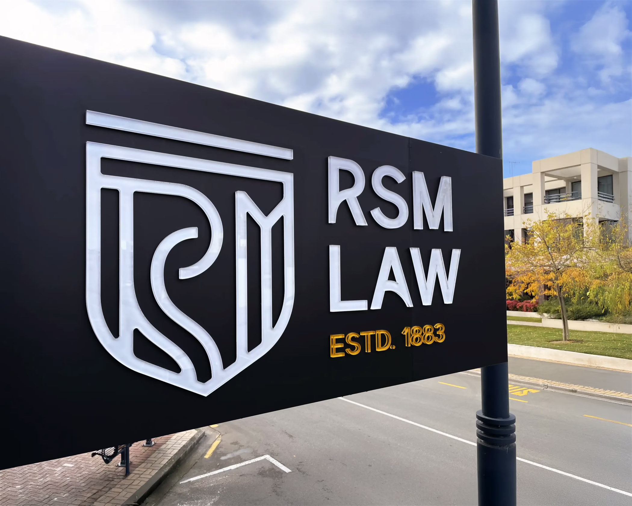A 3D exterior sign for RSM Law in Timaru, featuring raised white branding and gold lettering on a matte black background.