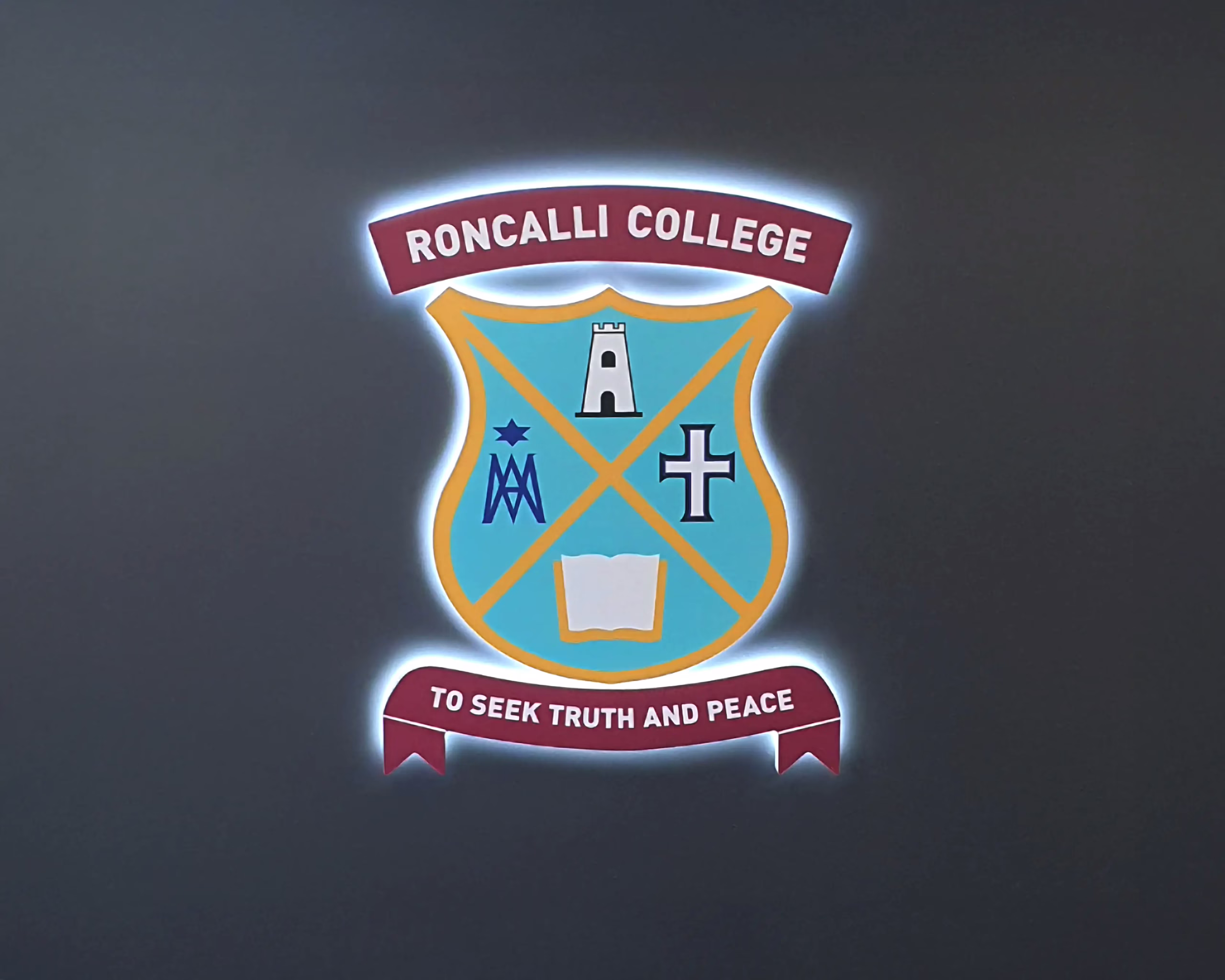Illuminated custom logo sign for Roncalli College featuring maroon crest and motto by Timaru Signs Graphix.