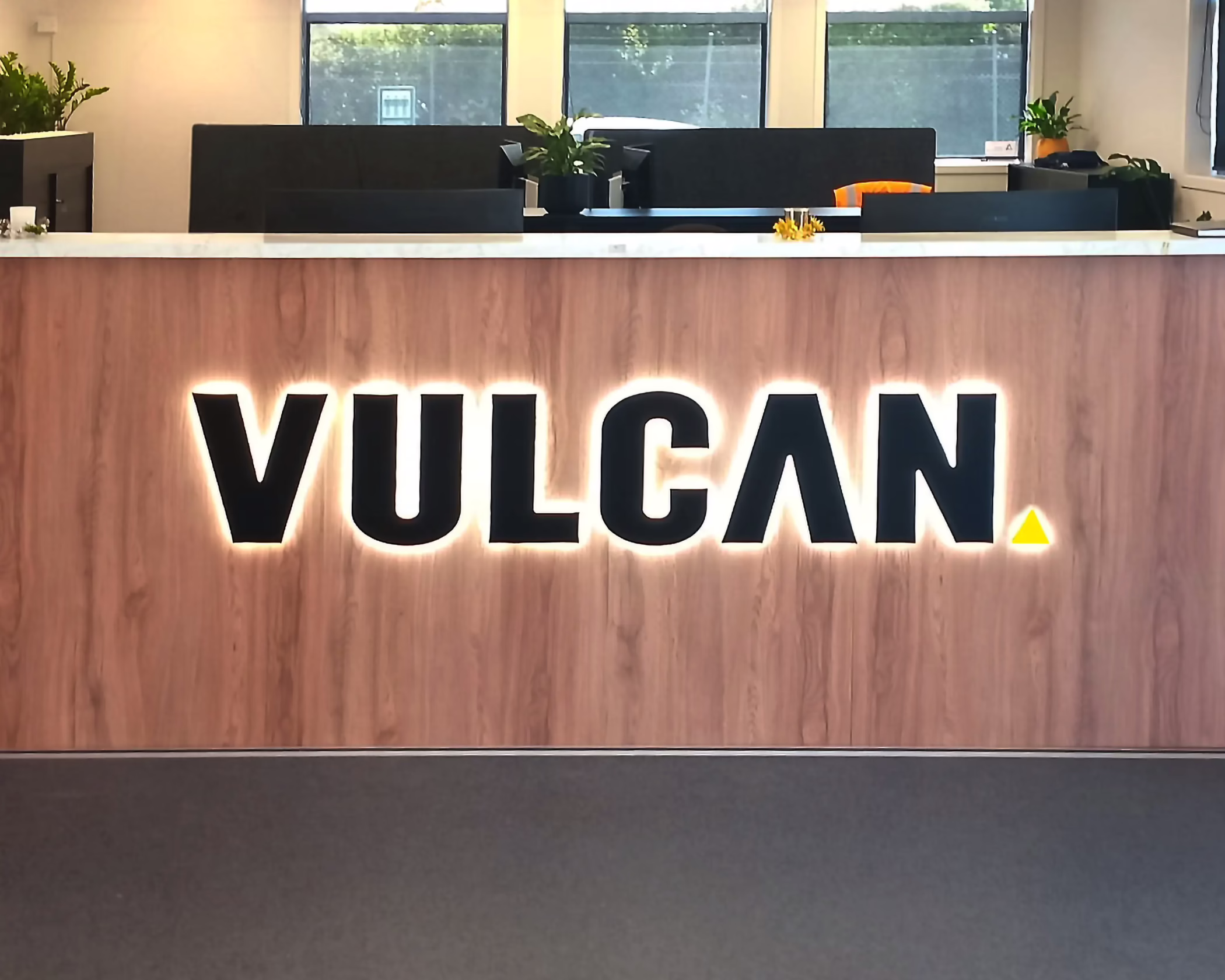 Halo-lit 3D custom reception sign for Vulcan on a wood panel desk by Timaru Signs Graphix.