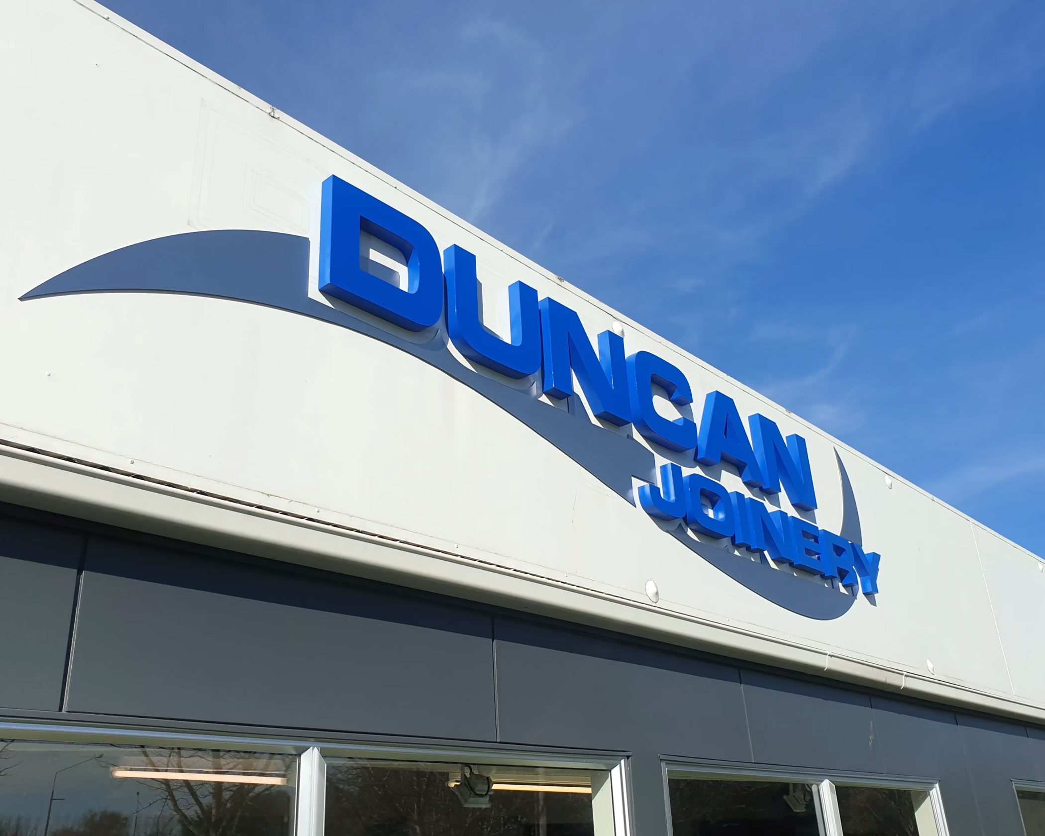 DUNCAN JOINERY exterior building fascia signage. Custom 3D letters, blue and grey swoosh graphic, white panels.