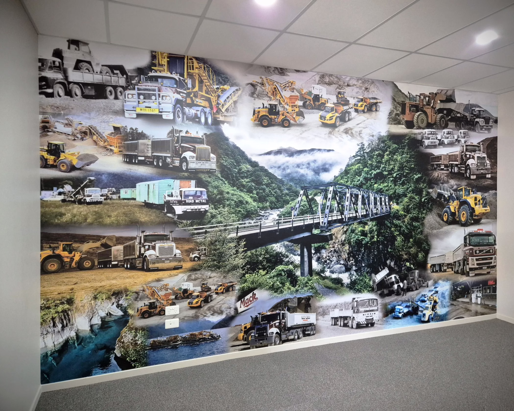 Custom floor-to-ceiling office mural for Road Metals featuring collage of heavy machinery and Mack trucks.