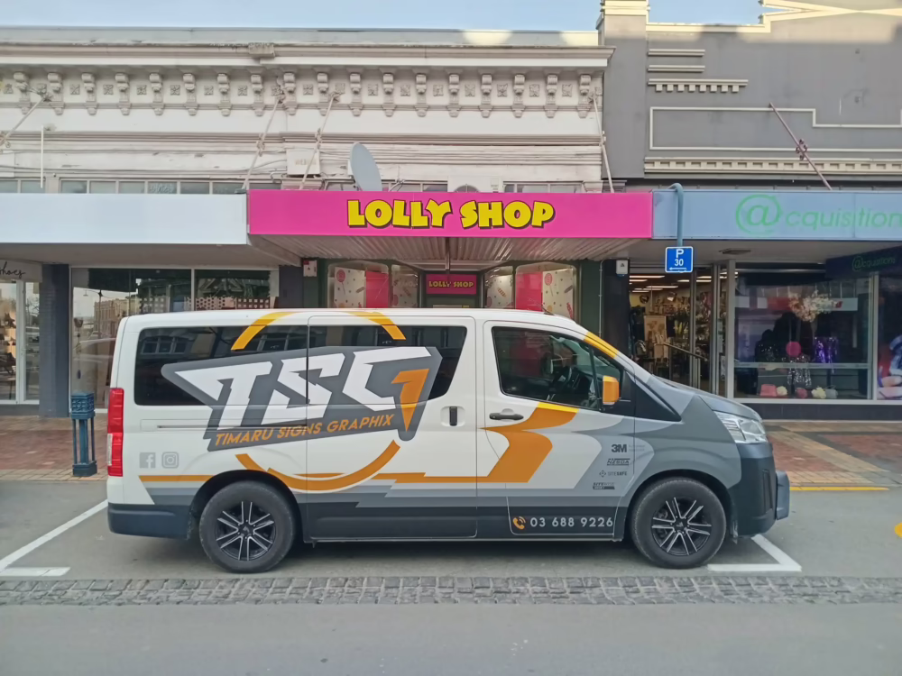Timaru Signs Graphix custom van wrap and building fascia signage for Lolly Shop on a Toyota Hiace, featuring 3M branding and contact info.