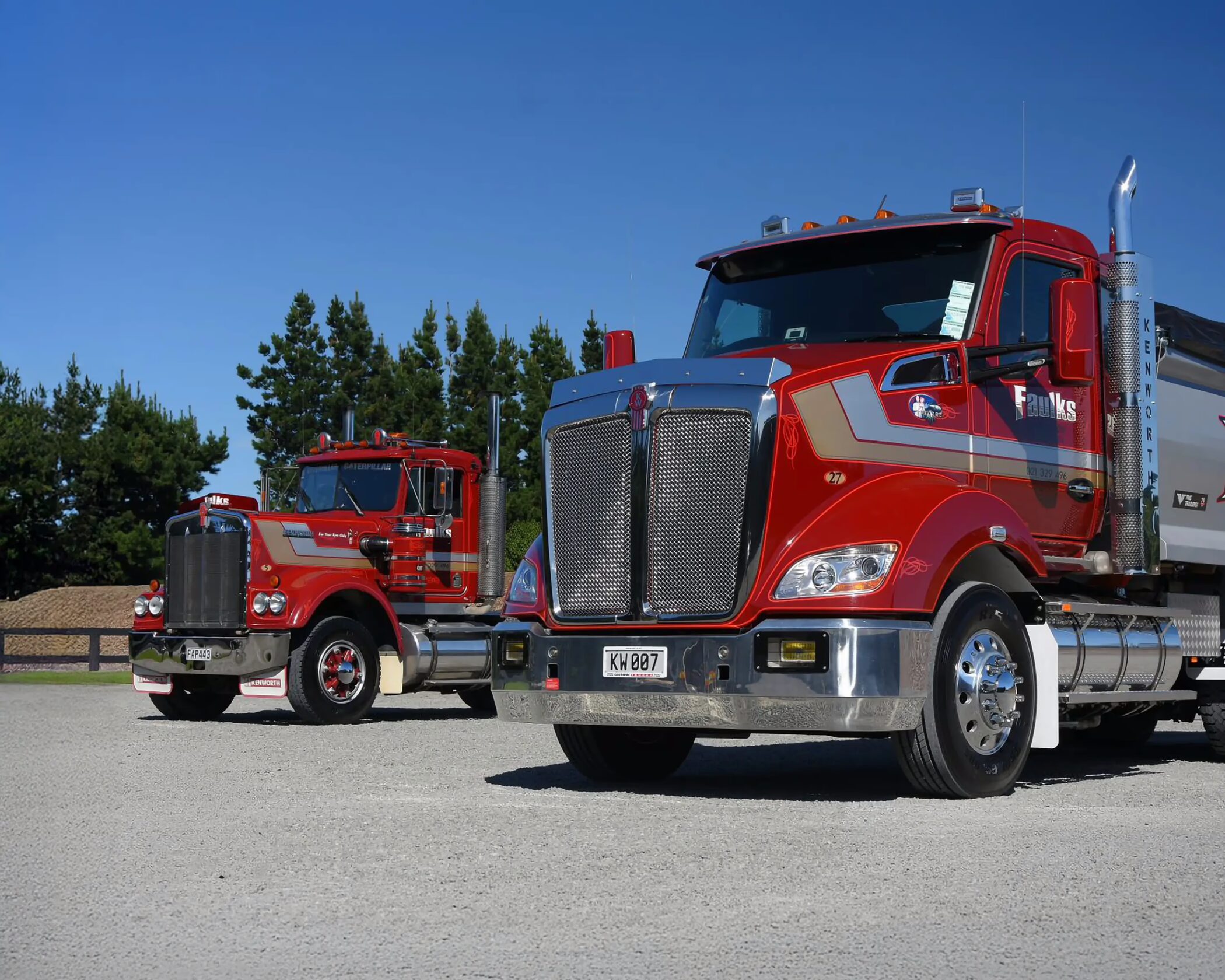 A modern red Kenworth truck with chrome trim and the license plate "KW 007" parked on a gravel lot in the foreground, with an older classic red Kenworth truck parked behind it. Both feature silver striping and "Faulks" branding on the cab.