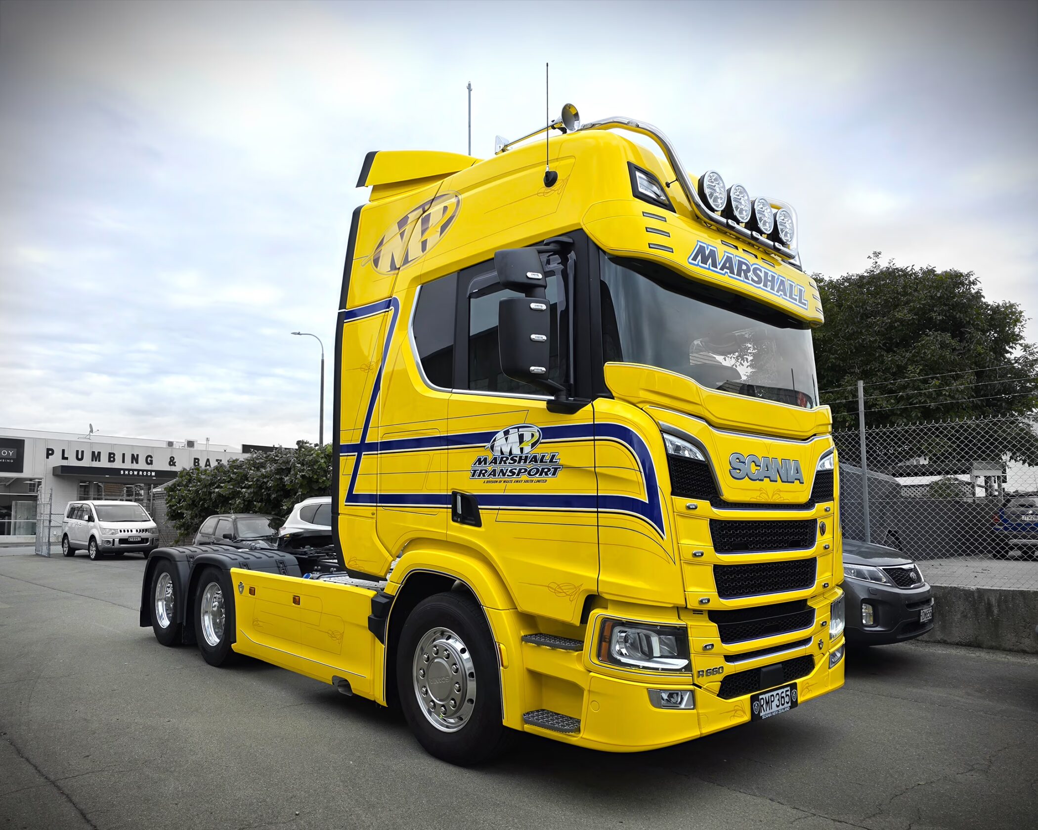 Bright yellow Scania R660 truck unit with custom blue and white Marshall Transport branding and roof-mounted spotlights, parked outdoors in an industrial area.