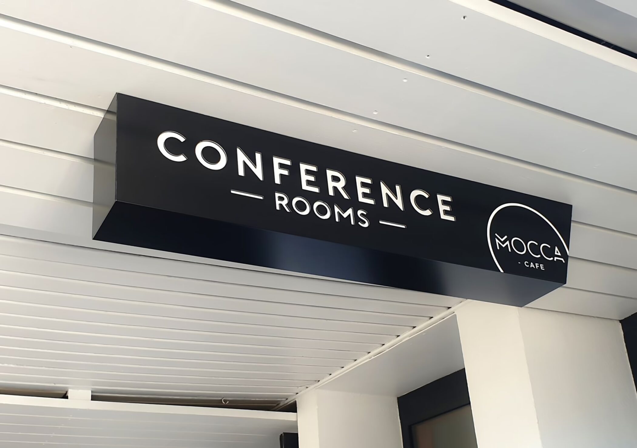 A black 3D sign mounted on an exterior soffit reading "CONFERENCE — ROOMS —" alongside the MOCCA Cafe logo.