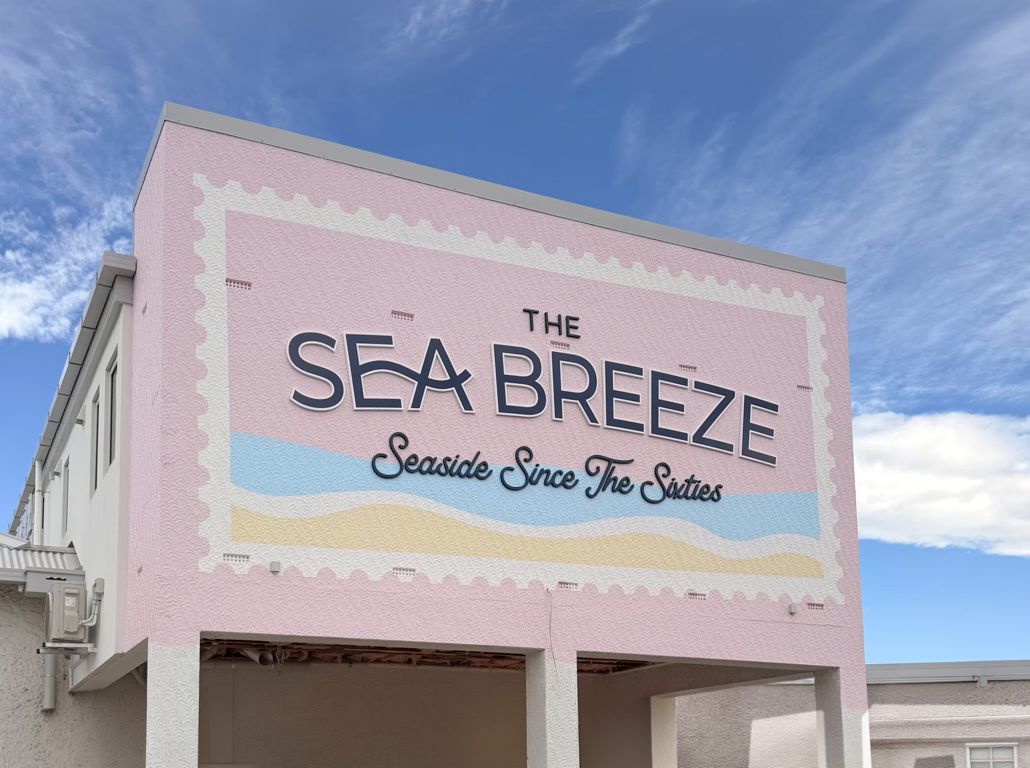 Custom pastel building fascia sign for The Sea Breeze, Timaru, featuring 1960s seaside waves design on a post-stamp background.