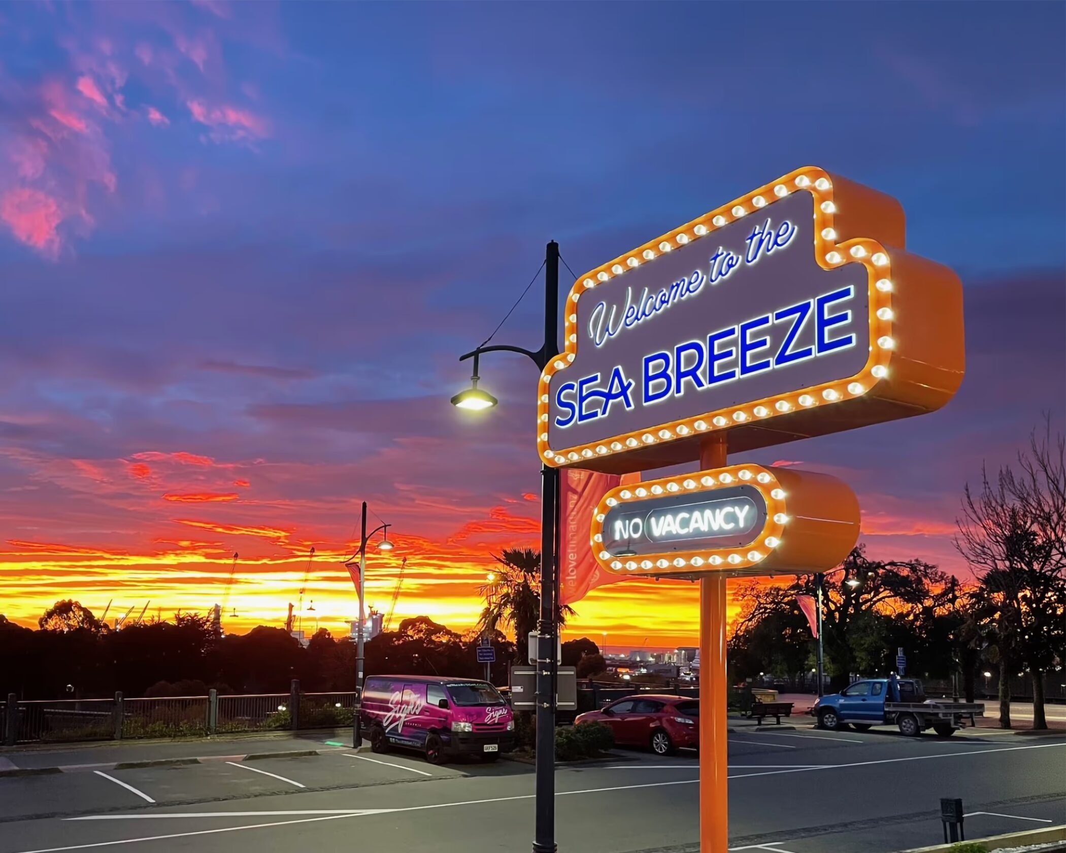 Illuminated vintage-style neon marquee sign for Sea Breeze in Timaru with glowing bulbs and custom retro lettering at sunset.