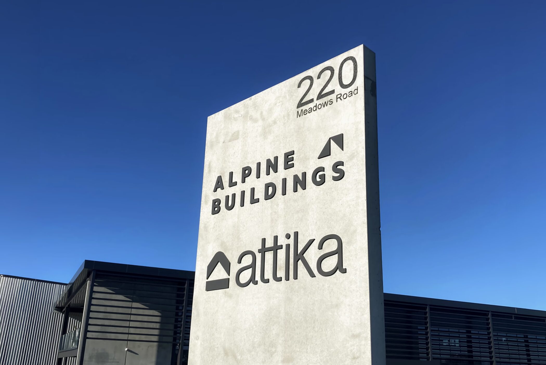 Large concrete freestanding sign at 220 Meadows Road Timaru with custom black lettering for Alpine Buildings and Attika.