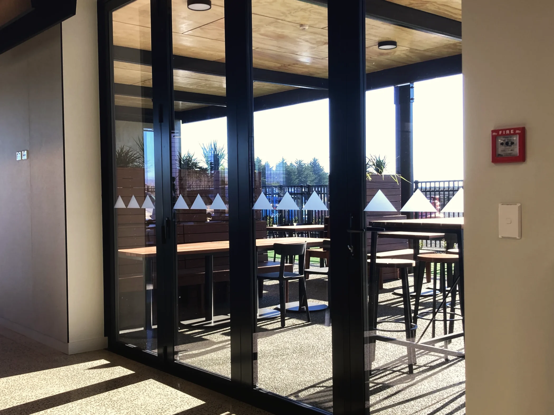 Frosted triangular window manifestation graphics applied at eye level across large glass bi-fold doors leading to an outdoor patio.