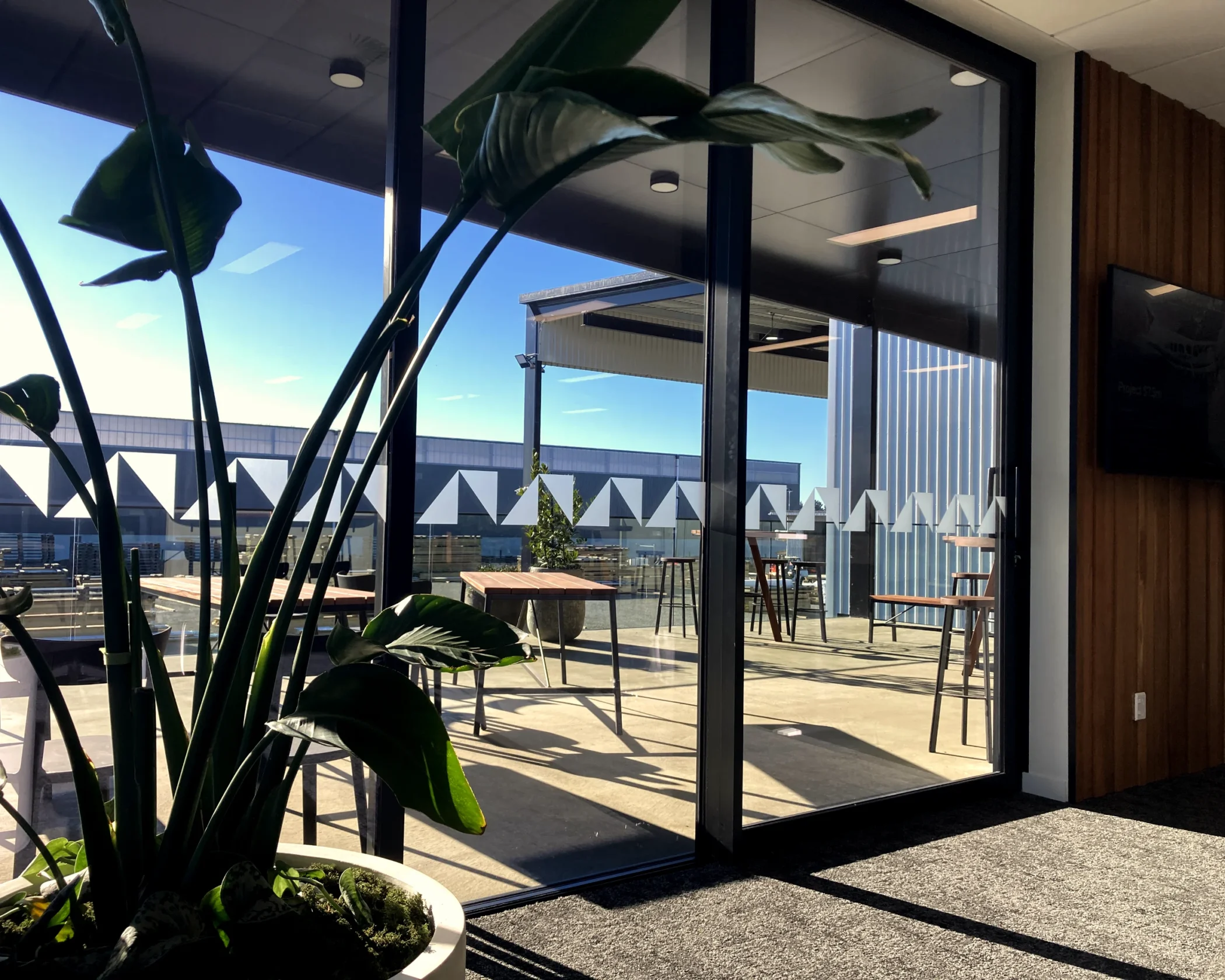 Large glass doors with frosted geometric triangle manifestation vinyl, opening onto an outdoor office balcony with high seating.