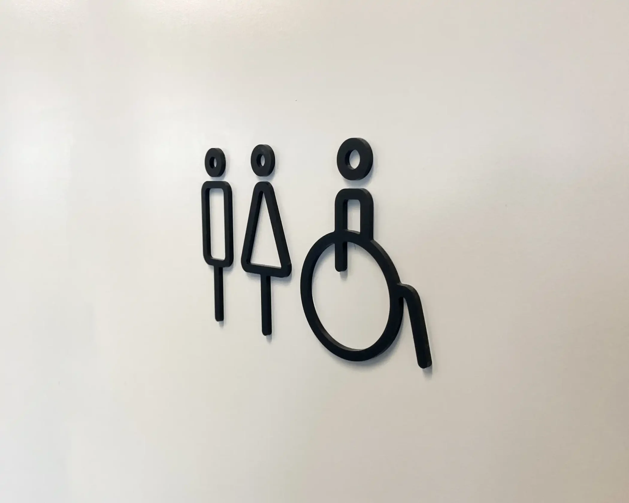 Black minimalist restroom signage on a plain white door featuring stylized icons for male, female, and accessible facilities.