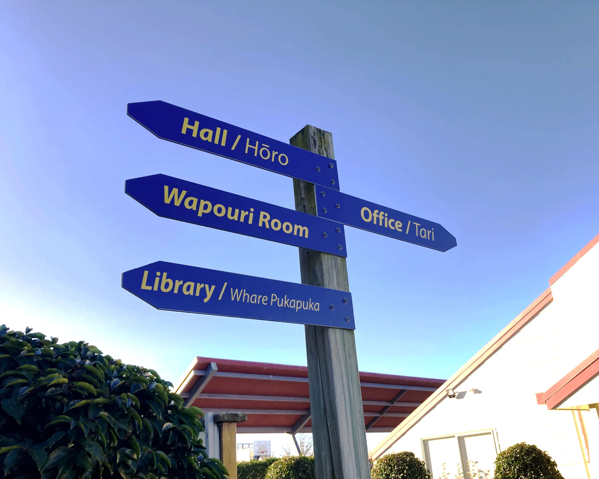 Directional post sign with blue arrow signs for Hall, Wapouri Room, Library, and Office for Bluestone School.