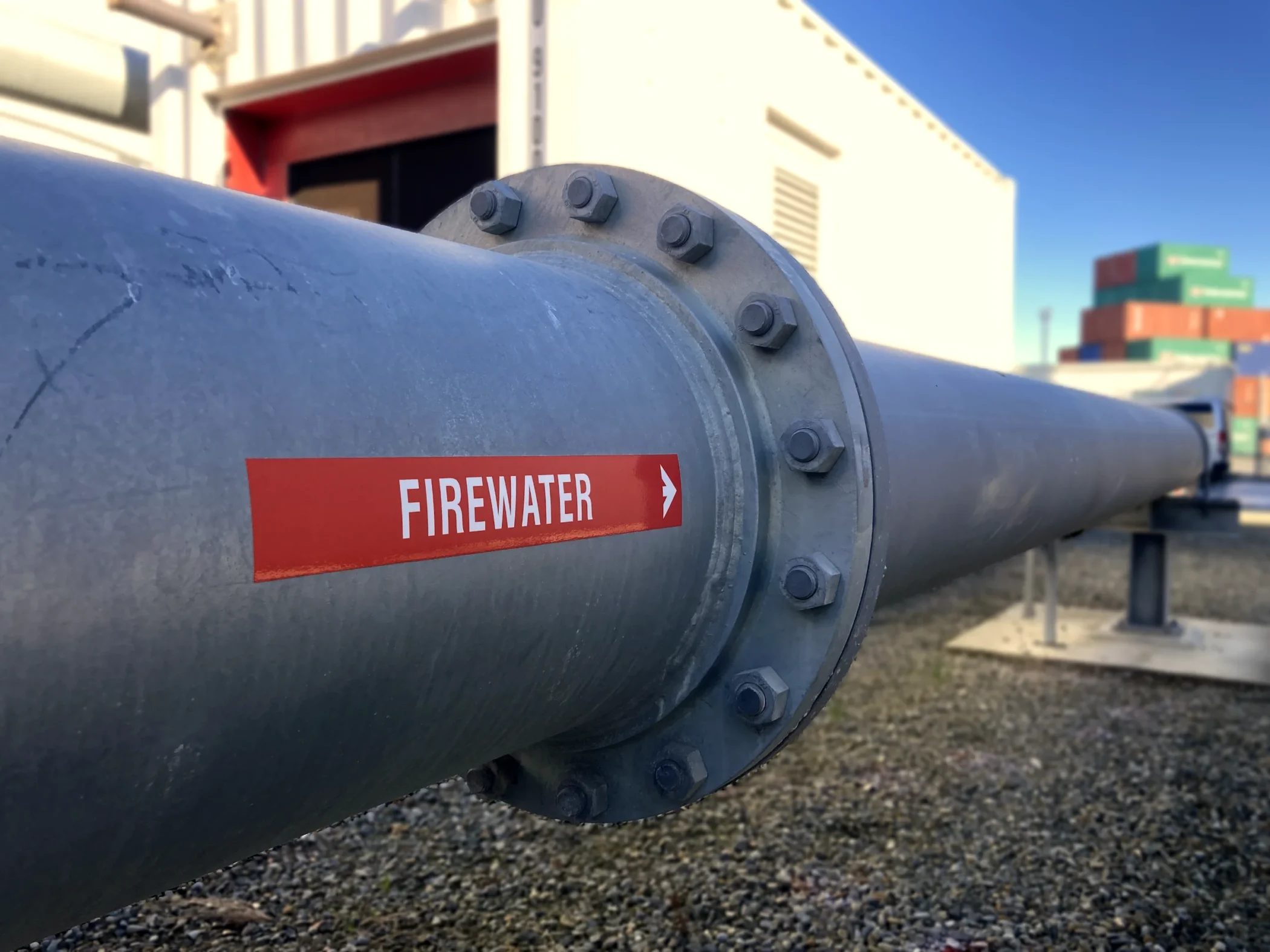 Red firewater directional pipe label sticker installed on industrial piping by Timaru Signs Graphix.